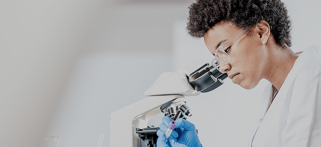 A woman in a lab coat and gloves looking through a microscope