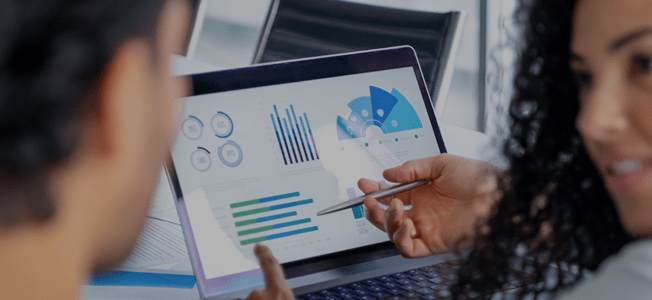 A man and woman look at a series of charts on a computer screen